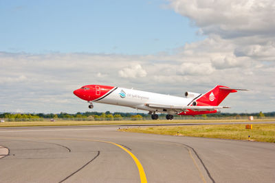 Red airplane on runway against sky