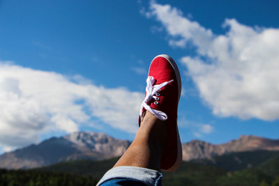 Low section of person wearing red shoes with feet up against mountains
