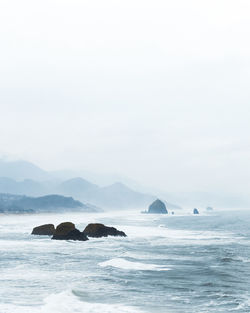 Rock formation in sea against sky during foggy weather