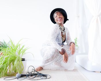 Smiling woman in dress looking away while crouching against white wall