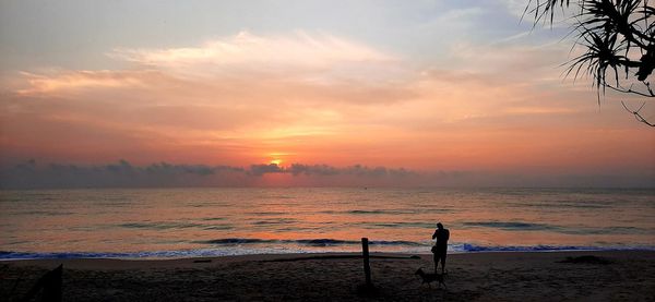 Silhouette person standing on beach against sky during sunset