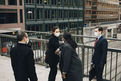 Female entrepreneurs doing elbow bump while standing with male colleagues on bridge in city during pandemic