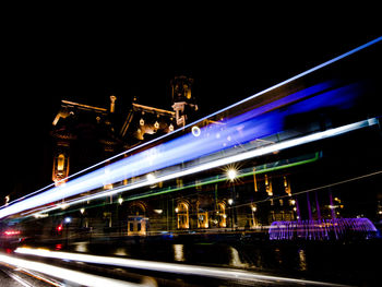 Light trails on illuminated city against sky at night