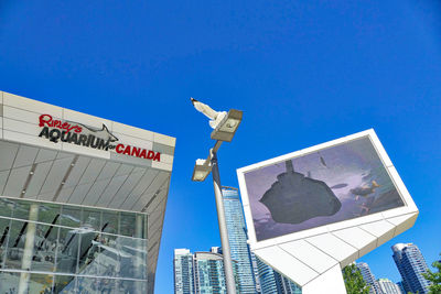 Low angle view of sign by building against clear blue sky