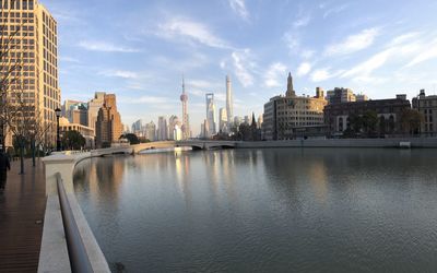 View of buildings by river against sky in city