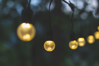 Low angle view of illuminated light bulb hanging against sky