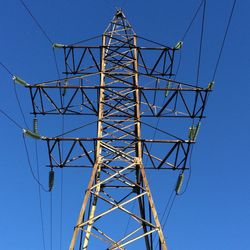 Low angle view of electricity pylon against clear blue sky