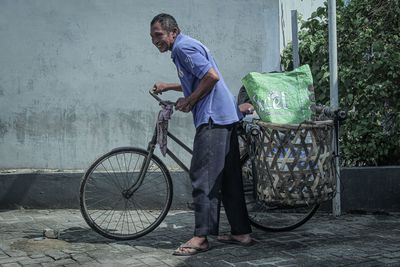 Side view of man with bicycle standing against wall