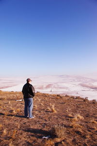 Rear view of man standing on field against clear sky during winter