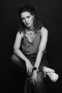 Portrait of young woman sitting against black background