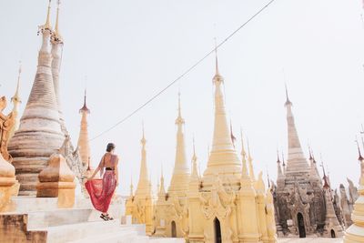 Rear view of mid adult woman standing by temples against clear sky