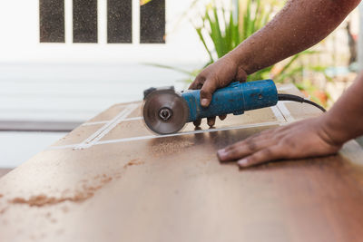 Hands of carpenter cutting piece of wood with electric circular saw.