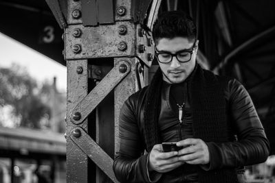 Young man using phone while standing at railroad station platform