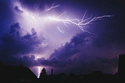 Lightning over silhouette buildings against sky