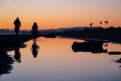 Silhouette men on lake against sky during sunset