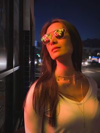 Close-up of beautiful woman wearing sunglasses standing outdoors at night