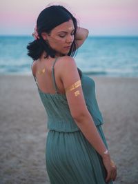 Young woman with flash tattoo standing at sandy beach