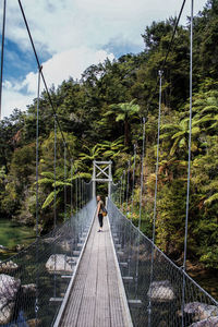 Side view of woman standing on footbridge in forest