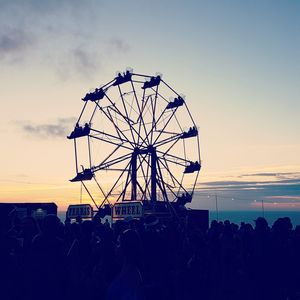 Silhouette ferris wheel by sea against sky during sunset