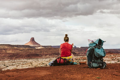 Sweaty female hiker sits on a backpack and eats an apple in utah