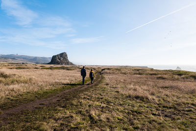 Rear view of men walking on landscape against sky