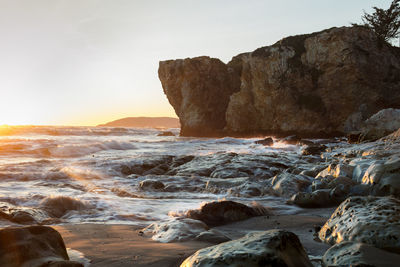 Rock formation on beach against sky during sunset