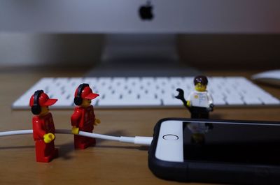 Close-up of figurines charging smart phone against computer on table