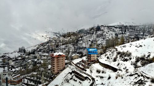 Ski lift by houses against sky during winter