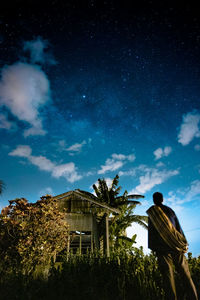 Rear view of man standing by building against sky at night