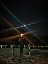 Rear view of woman standing on illuminated city against sky at night