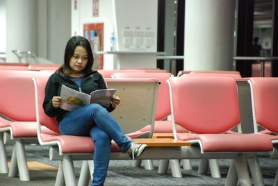 Young woman reading magazine on chair at airport