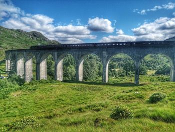 Arch bridge on field against sky