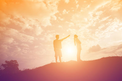 Silhouette couple standing against orange sky