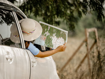 Rear view of woman reading map while leaning out from car window