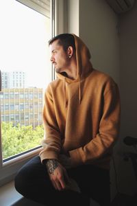 Young man looking through window while sitting at home