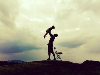 Full length of father holding daughter on field against cloudy sky