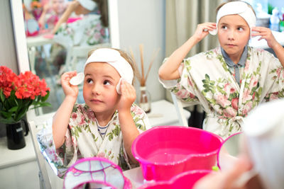 High angle view of girls cleaning face with cotton pad in spa