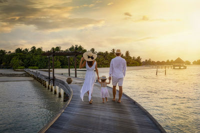 Rear view of couple walking at beach against sky