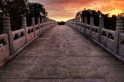 Walkway amidst trees against sky during sunset