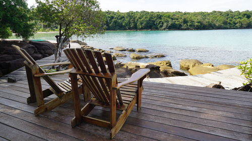 Adirondack chairs on floorboard against sea