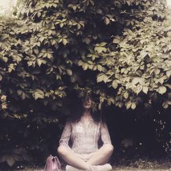 Woman sitting against plant