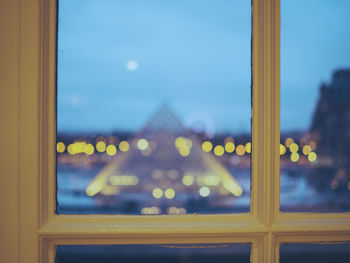 Illuminated louvre pyramid seen through window at dusk