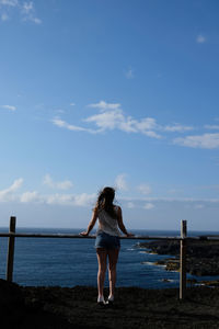 Rear view of woman standing by railing against sea and sky