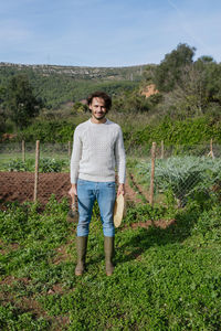 Young farmer standing in vegetable garden with straw hat and a hoe