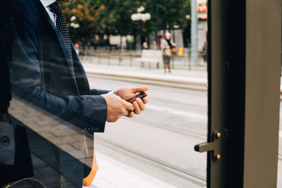 Midsection of mature businessman using smart phone seen from glass door