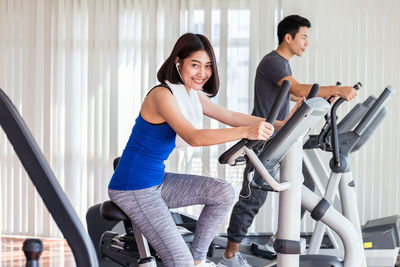 Portrait of smiling young woman with man exercising in gym