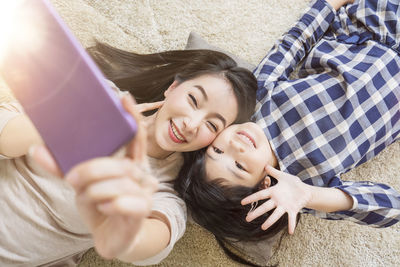 High angle portrait of mother and daughter taking selfie on mobile phone lying on bed