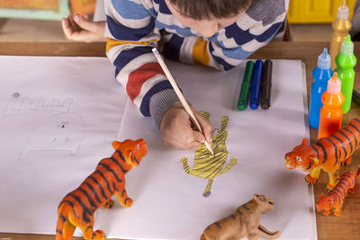 Boy sitting at a table drawing a tiger.