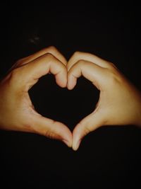 Close-up of man making heart shape against black background