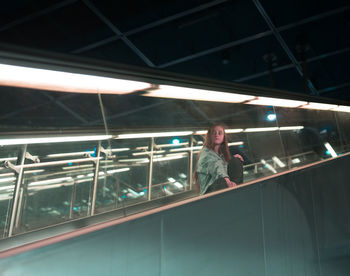 Woman sitting on escalator in city at night